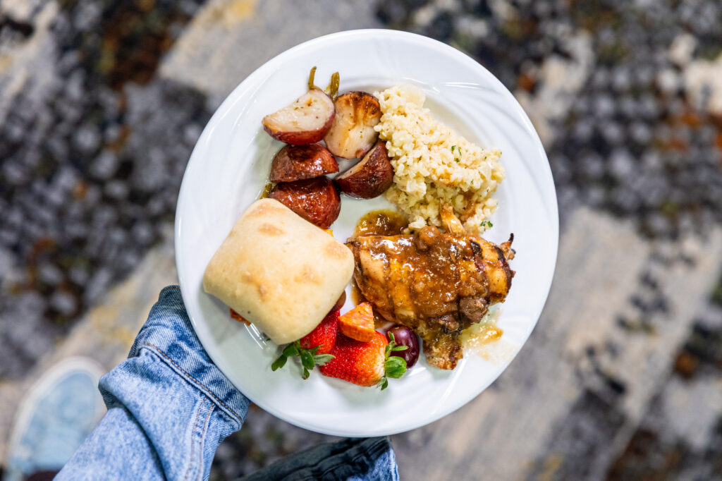 Image of a plated meal with meat, rice, bread, fruit, and potatoes